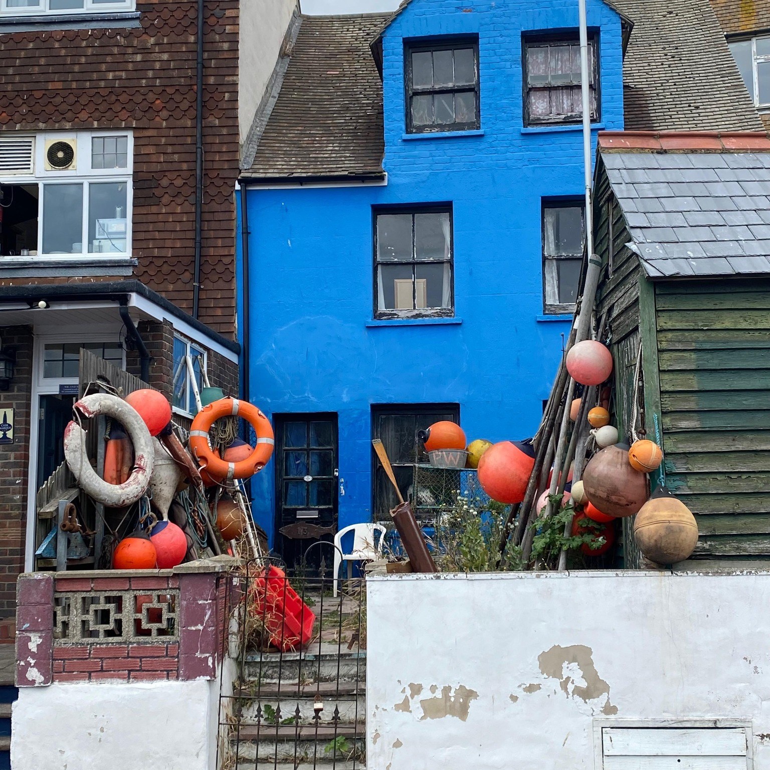 Bright blue painted fisherman's house with orange floats and gear in front, Hastings UK