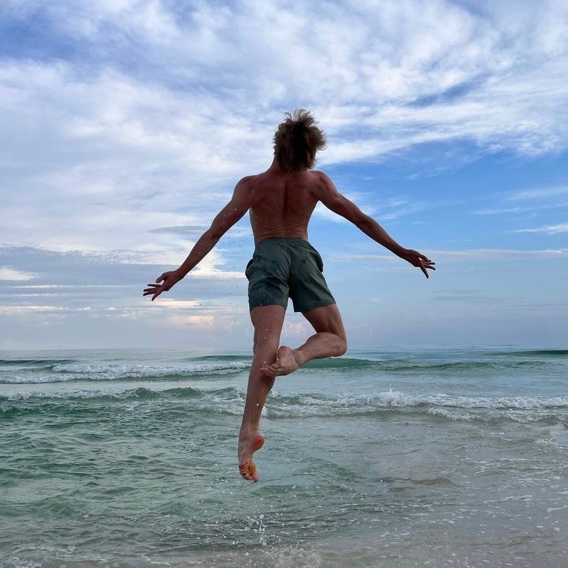 Professional male ballet dancer leaping above waves in Gulf of Mexico