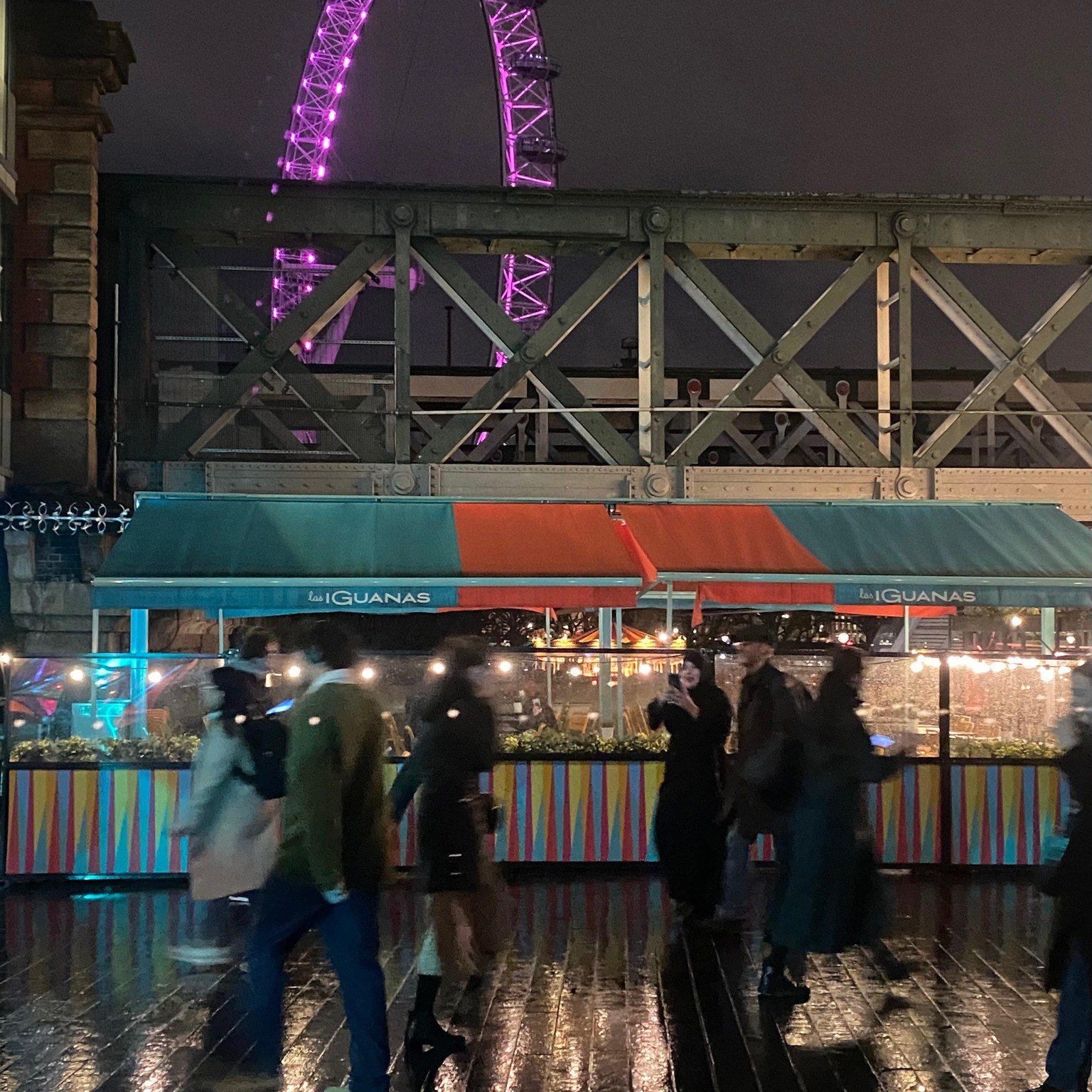 Rainy night with muted lights reflecting off Southbank sidewalk along the Thames in London.