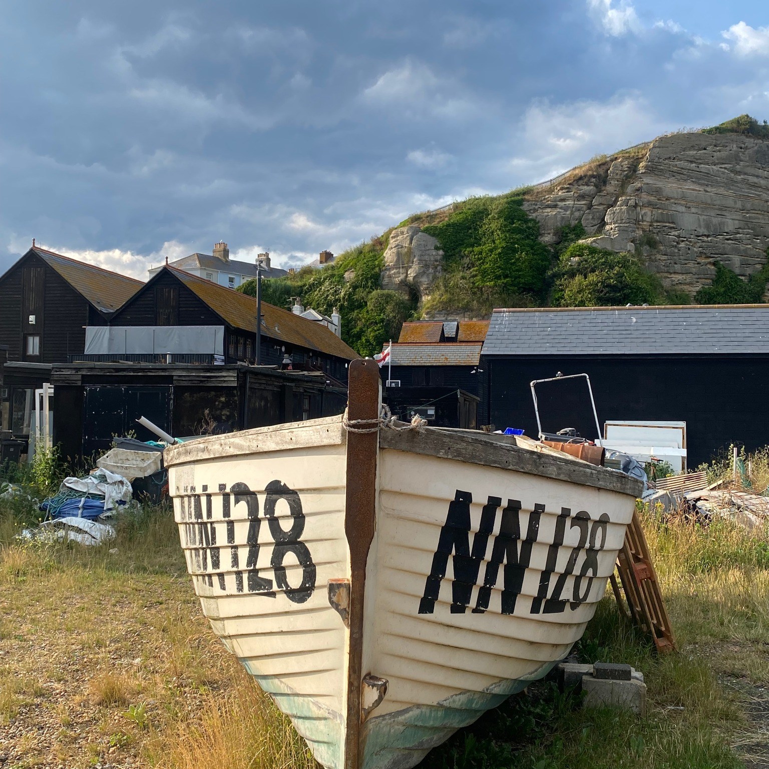 Longview of wooden boat sitting ashore amid grass and sand.