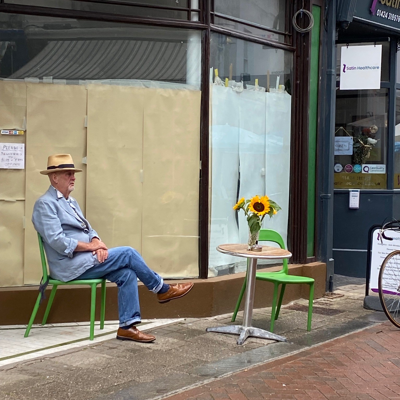 Man in a straw hat sitting outside an old shop in Old Hastings Town