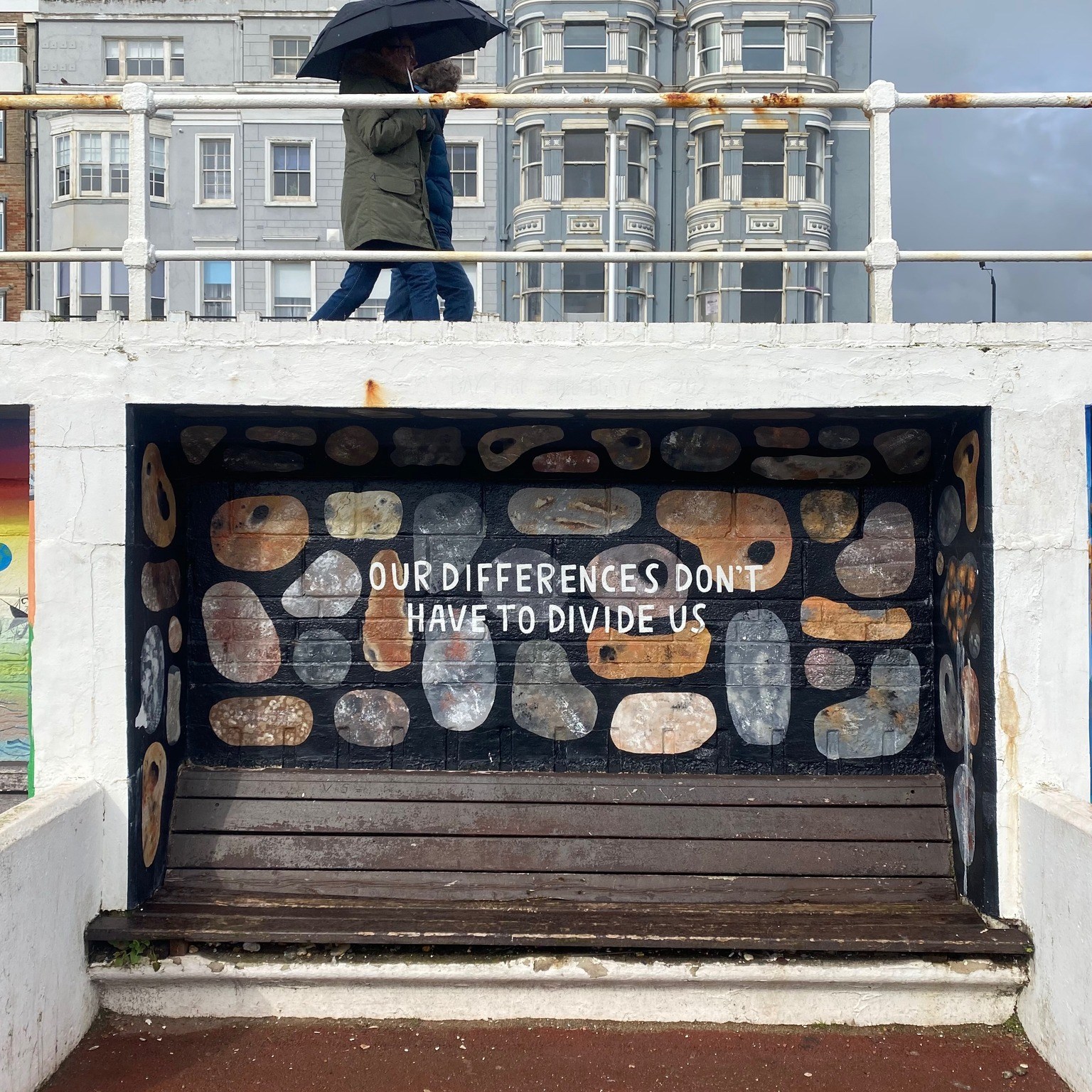 St Leonards walkway with view of couple walking under and umbrella and bench with mural.
