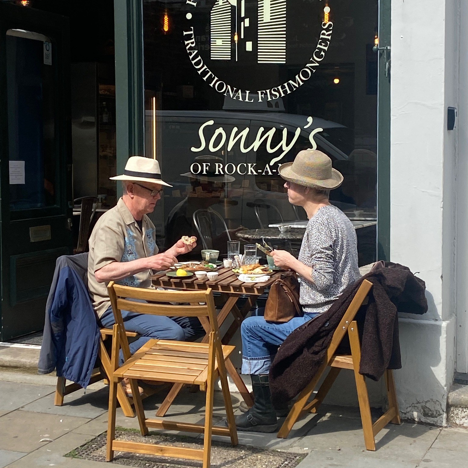 Two men wearing summer straw hats and dining outside Sonny's fish cafe.